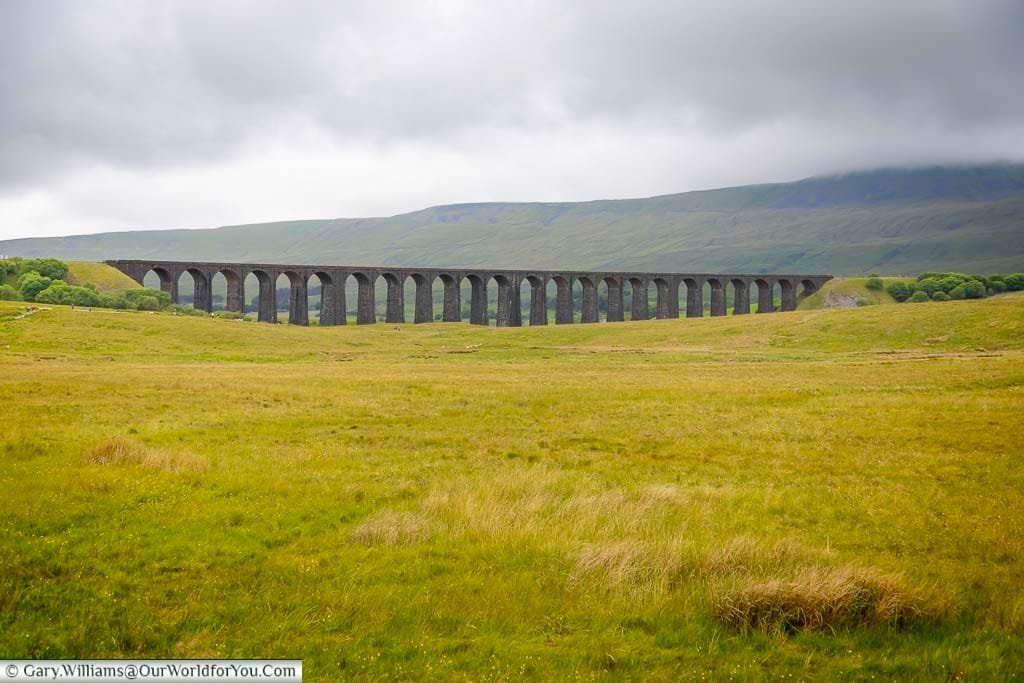 A dramatic view of the Ribblehead Viaduct stretching across the Yorkshire Dales, with its 24 towering stone arches set against rolling hills and moody skies. This iconic railway landmark is a must-see destination for history enthusiasts and walkers exploring the natural beauty of North Yorkshire.