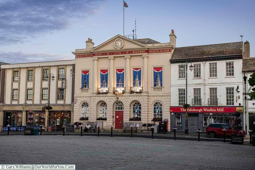A charming view of Ripon Town Hall in North Yorkshire, adorned with red, white, and blue drapes and surrounded by quaint shops and cobbled streets. This historic market town blends tradition and heritage, making it a picturesque stop on any Yorkshire road trip.