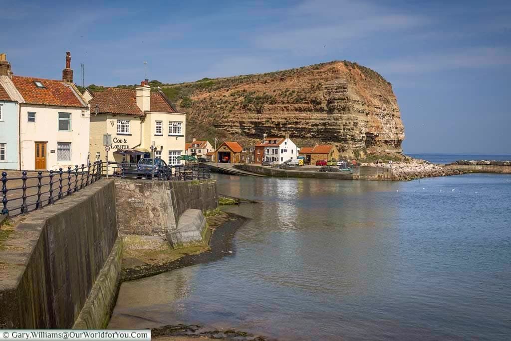 A tranquil view of the charming fishing village of Staithes in Yorkshire, featuring quaint cottages, the iconic Cod & Lobster pub, and dramatic coastal cliffs meeting the sea. This hidden gem on the Yorkshire coast is perfect for those seeking scenic beauty, maritime history, and peaceful seaside escapes.
