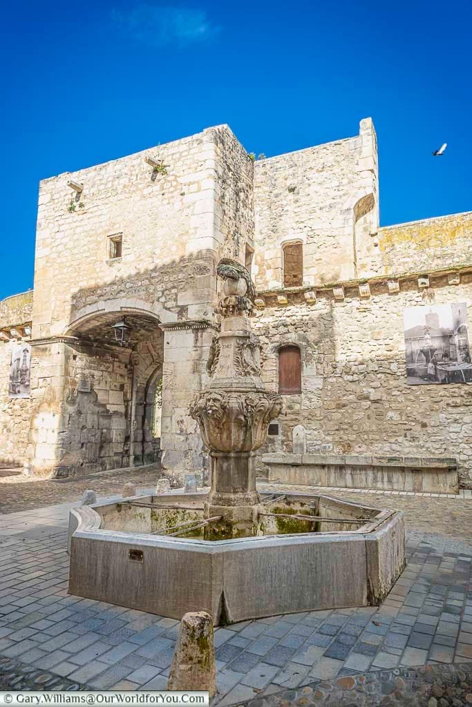 The Cormoran Fountain in Pernes-les-Fontaines, Provence, stands in front of a historic stone gateway, offering a glimpse into the town's medieval charm. This beautifully carved fountain is one of the town’s many water features and a highlight of any cultural road trip through southern France.