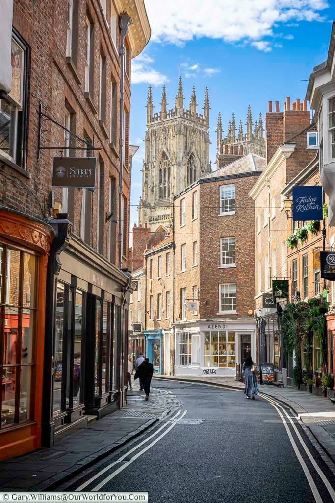 A charming view of Low Petergate in York with its historic brick shops and the magnificent York Minster towering above. This picturesque street perfectly captures the blend of medieval architecture and vibrant city life in York.