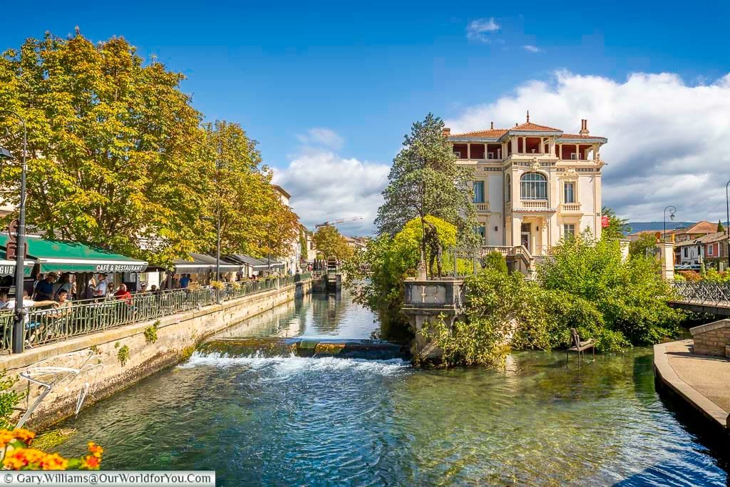 The iconic Maison René Char overlooks the tranquil Sorgue River in L’Isle-sur-la-Sorgue, surrounded by leafy trees and bustling riverside cafés. This picturesque Provençal townscape blends cultural heritage with vibrant local life, making it a must-see destination in southern France.