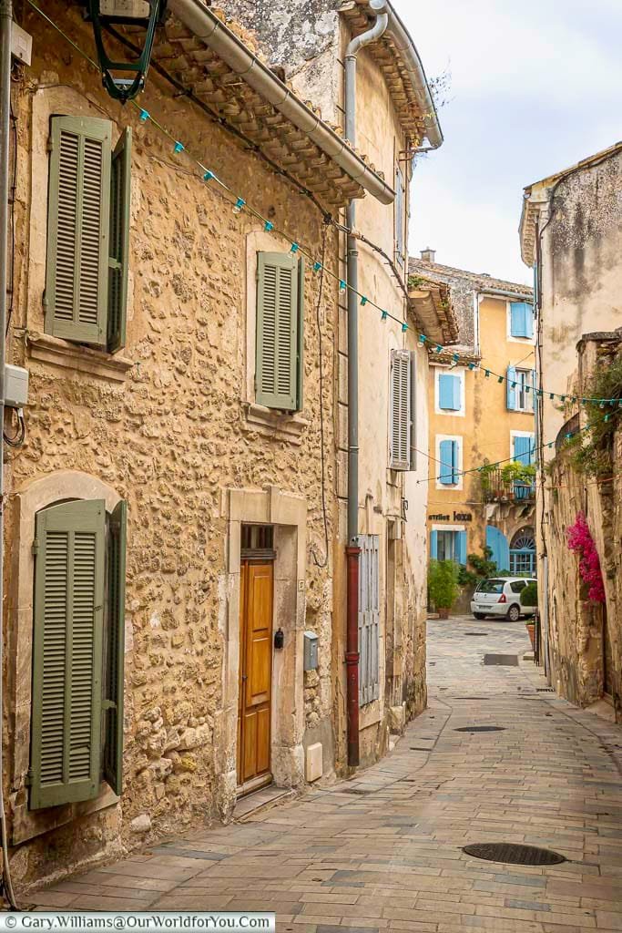 Charming narrow street in a Provençal village, lined with stone houses featuring pastel shutters and festooned with hanging lights. This picturesque alleyway captures the timeless appeal and tranquil ambiance of southern France’s hidden gems.