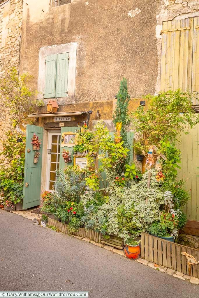Charming house entrance in Saignon, Provence, adorned with lush greenery, colorful flowers, and rustic green shutters. This picturesque corner captures the authentic village atmosphere and floral beauty of southern France’s most enchanting destinations.