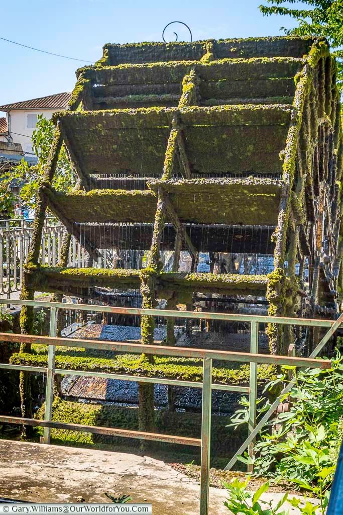A moss-covered waterwheel gently turns in the sunlight beside a peaceful river in L’Isle-sur-la-Sorgue, one of Provence’s most picturesque villages. This charming relic of the town’s industrial past adds character to a popular stop on a French road trip through southern France.