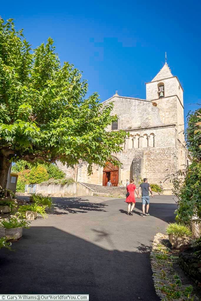 Visitors approach the historic Notre-Dame de Pitié church in Provence, framed by lush greenery and set against a vibrant blue sky. This Romanesque gem is a must-see landmark on any cultural or heritage tour of southern France.