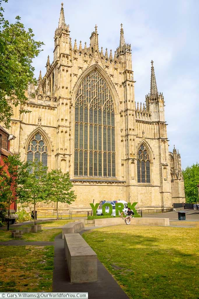 The stunning west front of York Minster with its grand Gothic windows, seen from the gardens with a decorative York sign in the foreground. This iconic landmark is one of the top attractions in York, England, and a must-visit for history lovers.