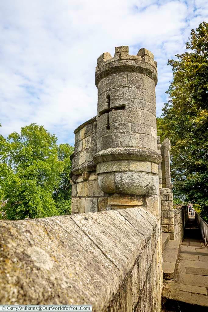 A close-up view of the historic stone walls and tower along York’s medieval city walls, featuring a cross-shaped arrow slit. This iconic walkway offers visitors a chance to explore York’s rich history while enjoying panoramic views of one of England’s most beautiful cities.