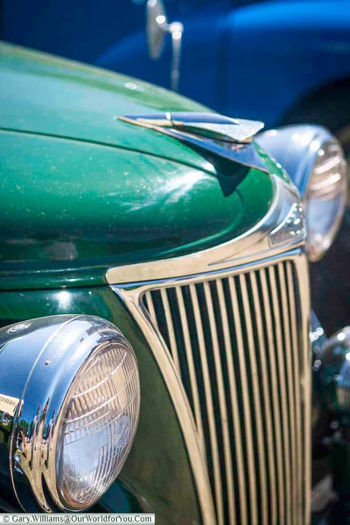 The gleaming front end of a classic green vintage car captures the sunlight at the Kent County Show's heritage vehicle display. Chrome detailing and retro curves add to the timeless automotive allure.