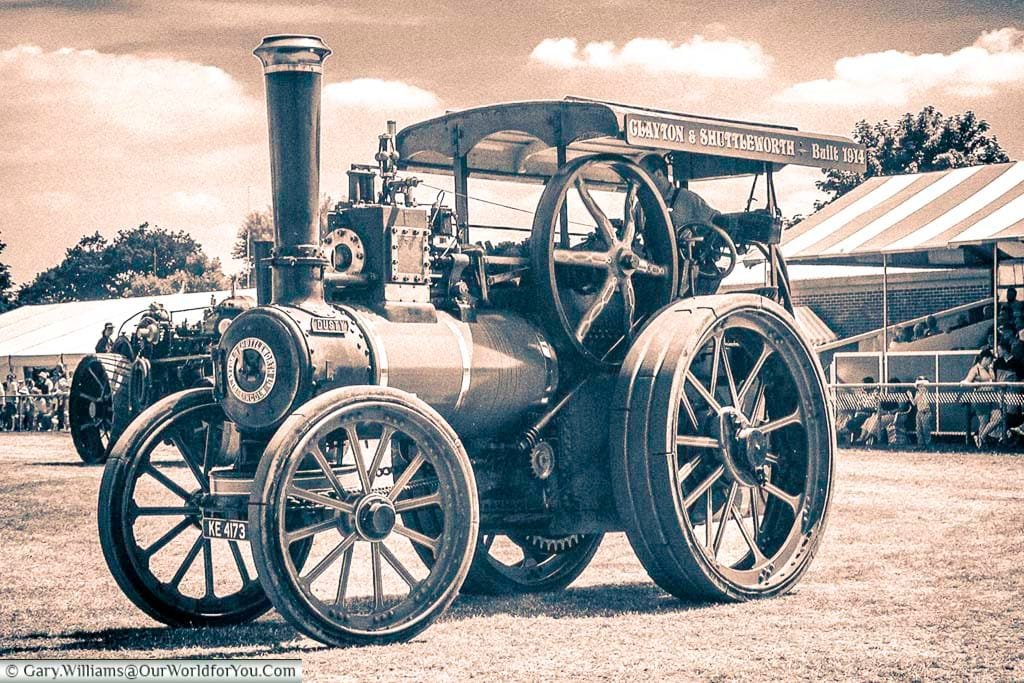 Sepia-toned photo of a 1914 Clayton & Shuttleworth steam traction engine proudly displayed at a traditional English County Show. This nostalgic scene captures the enduring charm of vintage rural machinery and its place in UK heritage events.