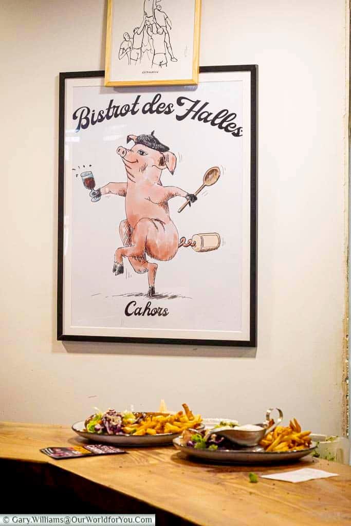 Interior view of Bistrot des Halles in Cahors with a whimsical pig illustration and plates of French food on a rustic table. This beloved local eatery offers an authentic taste of southern French cuisine in a relaxed and quirky setting.