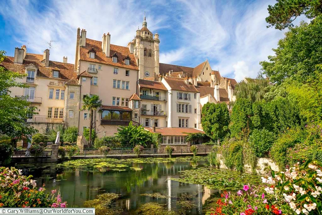 The picturesque Canal des Tanneurs flows through the historic town of Dole in Burgundy, framed by flowers and medieval buildings. This tranquil scene showcases one of France's hidden gems, rich in charm and cultural history.