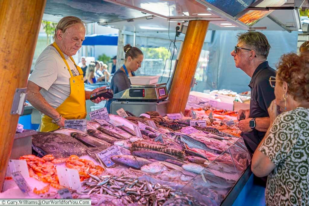 A bustling seafood stall at Sanary-sur-Mer’s outdoor market displays freshly caught Mediterranean fish and shellfish. Locals queue to chat with the fishmonger and select their day’s catch in this vibrant coastal town.