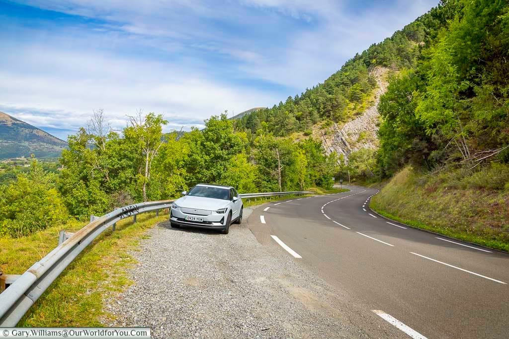 A Polestar 2 EV pauses on a scenic mountain road surrounded by forested slopes and rugged cliffs in the French Alps. This image captures the freedom and sustainability of touring France in an electric vehicle.