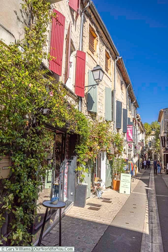 Charming old stone houses with colourful shutters line a sunny pedestrian street in Saint-Rémy-de-Provence, brimming with vines and local boutiques. This quintessential Provençal town offers a perfect blend of history and vibrant local life.