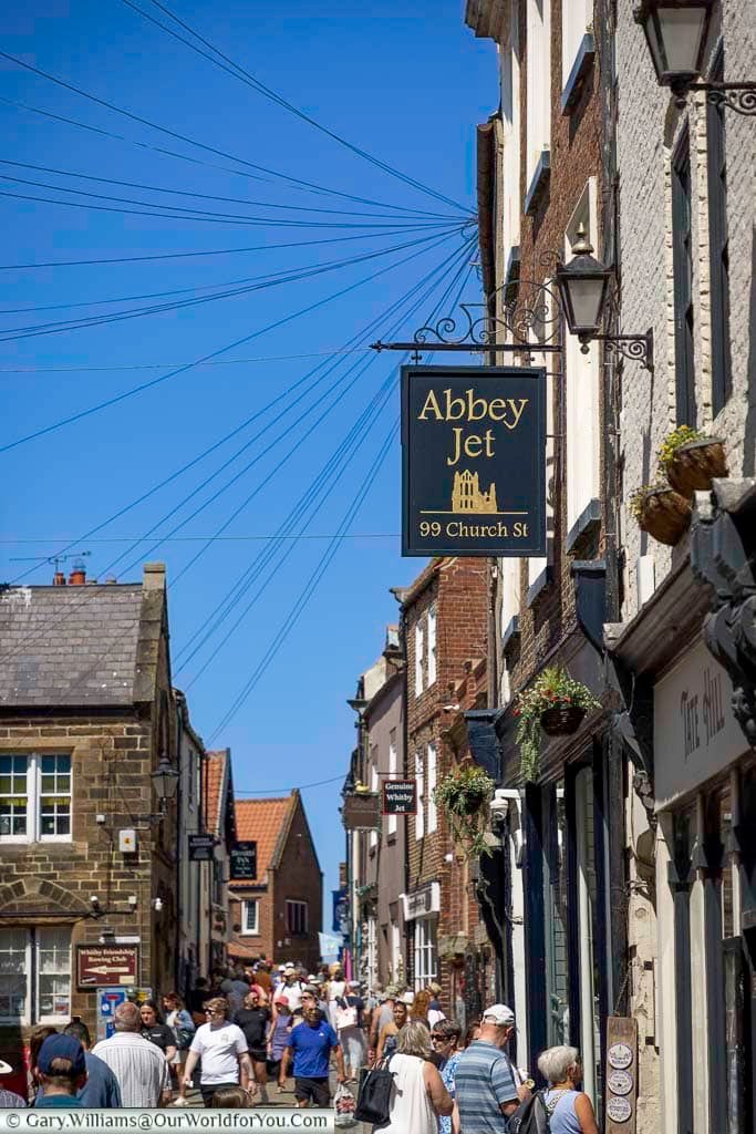 A lively street in Whitby packed with visitors and independent shops, with the iconic Abbey Jet sign overhead. Church Street buzzes with charm and is a must-visit for jet jewellery and local heritage.