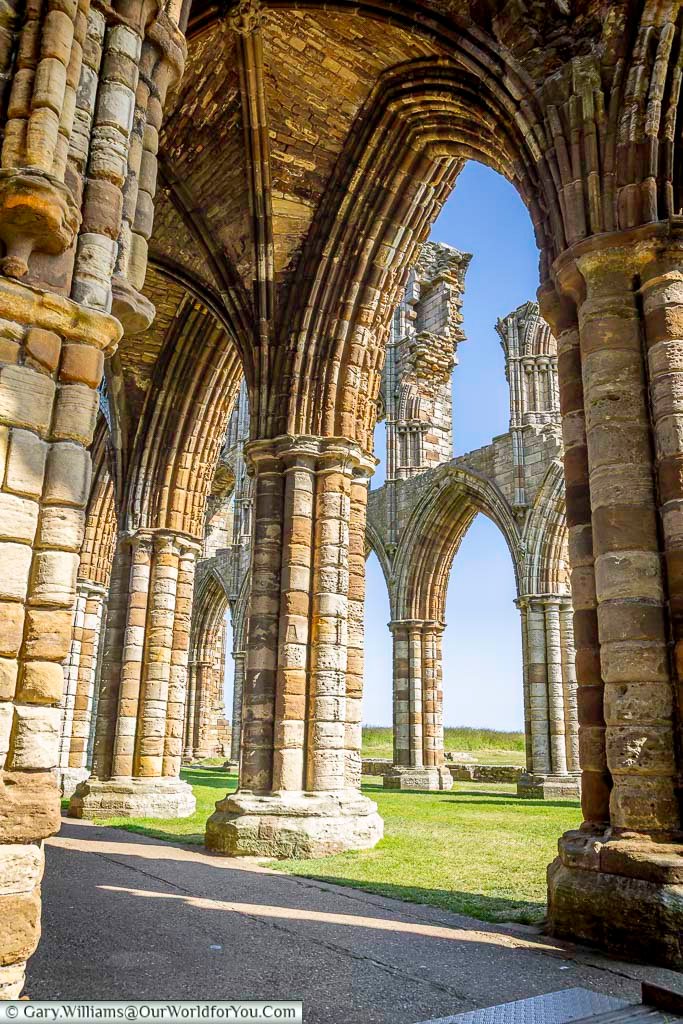 A detailed look through the ribbed stone arches of Whitby Abbey reveals the grandeur of its medieval architecture. Sunlight filters through the ruins, highlighting the historic craftsmanship of this iconic landmark.