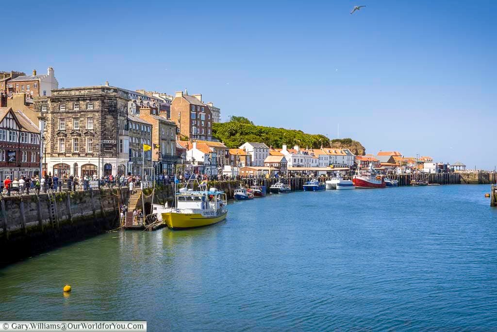 A busy scene along Whitby’s harbourfront with colourful fishing boats, heritage buildings, and crowds enjoying the Yorkshire coast. This vibrant quayside is a hub of activity and local charm.