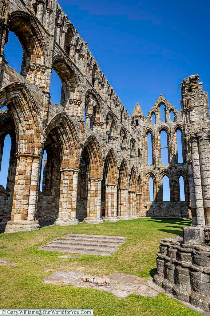 The towering Gothic arches and intricate stonework of Whitby Abbey reveal the grandeur of this medieval ruin against a vibrant blue sky. A must-see historic landmark in Yorkshire, perfect for architecture and history lovers.