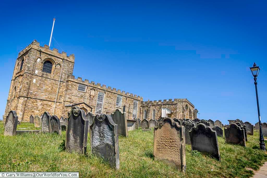 A sloping churchyard leads to the historic St Mary’s Church in Whitby, with weathered gravestones and striking medieval architecture under a cloudless sky. This atmospheric scene inspired Bram Stoker's Dracula and attracts visitors year-round.
