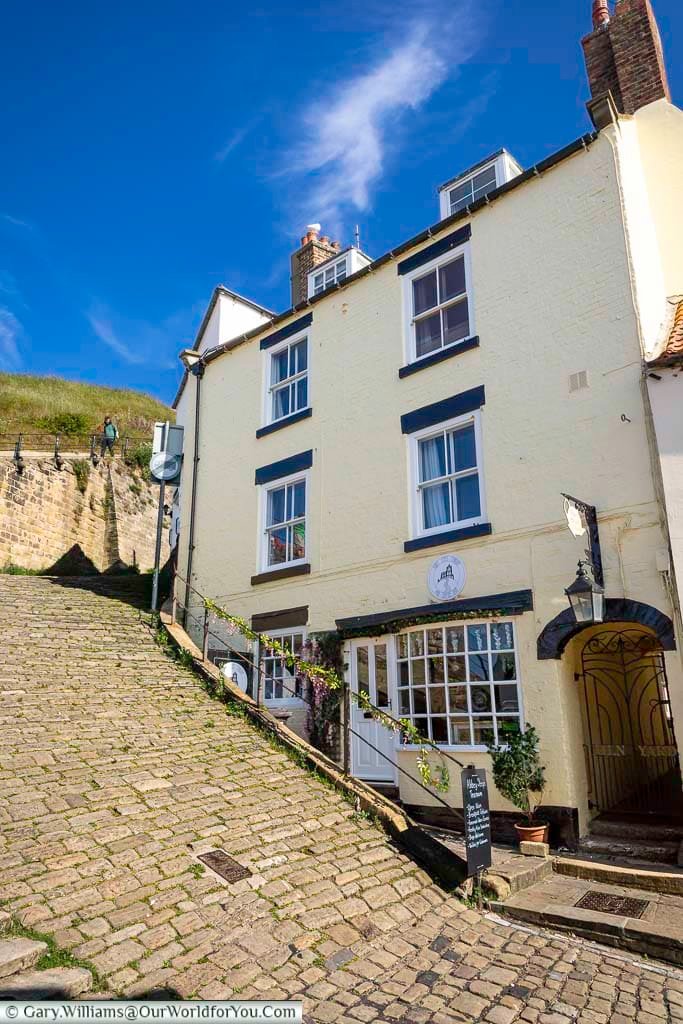 A view looking up the cobbled start of the 199 Steps in Whitby, with a traditional tearoom nestled along the historic route. This iconic climb leads to St Mary’s Church and the dramatic ruins of Whitby Abbey above the town.