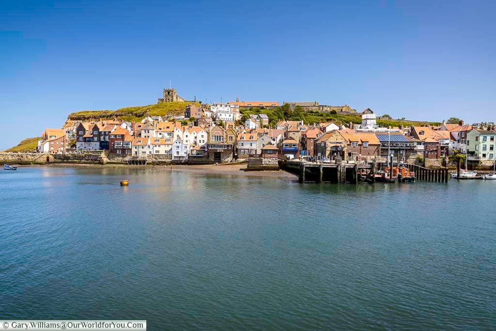 Charming cottages line the base of Whitby’s East Cliff, topped by St Mary’s Church and the famous Abbey ruins. This classic view showcases the town’s unique topography and layered history.