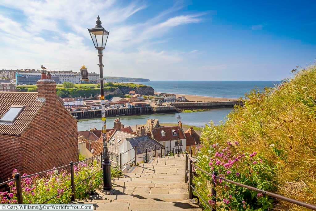 A panoramic view over the west side of Whitby from the top of the 199 Steps, with the River Esk meeting the North Sea. Colourful rooftops and a golden beach complete this classic Yorkshire coastal scene.