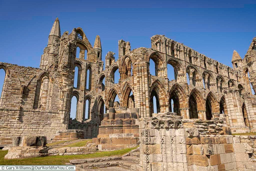A close-up view of the majestic ruins of Whitby Abbey, showcasing its towering Gothic arches and detailed medieval stonework under a clear blue sky. This iconic Yorkshire landmark stands as a powerful reminder of Whitby’s religious and cultural heritage.