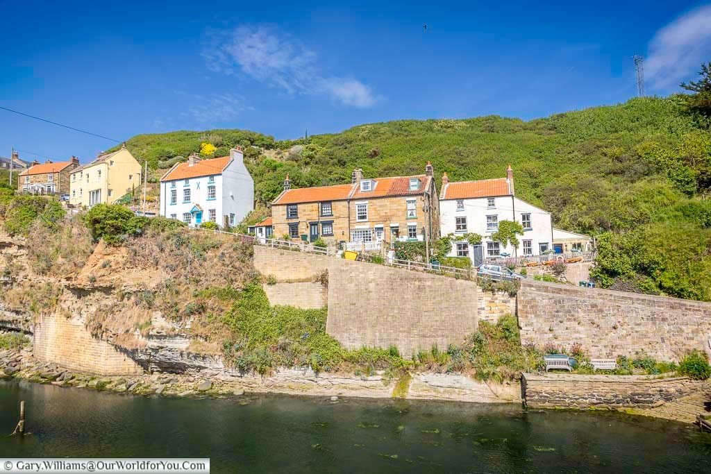 A row of charming hilltop cottages on Cowbar Bank in Staithes overlook the meandering beck and the North Sea beyond. The lush green surroundings and traditional stonework reflect the rugged beauty of Yorkshire’s coastline.