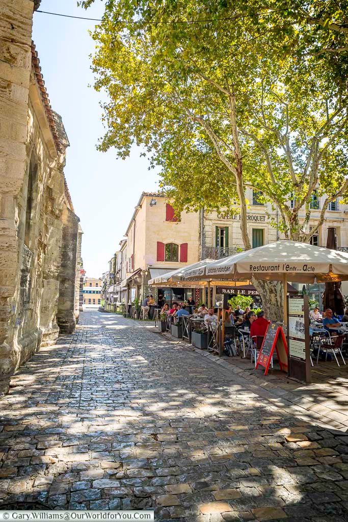 A quiet cobbled street in Aigues-Mortes bathed in dappled light, with cafés and historic façades creating a timeless southern French ambiance. Explore the charming backstreets of this medieval town in Occitanie.