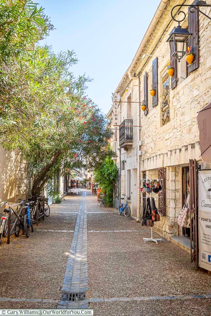 Bicycles lean against stone buildings on a peaceful lane in Aigues-Mortes, lined with artisan boutiques and flowering trees. Discover the timeless charm of this medieval walled town in southern France.