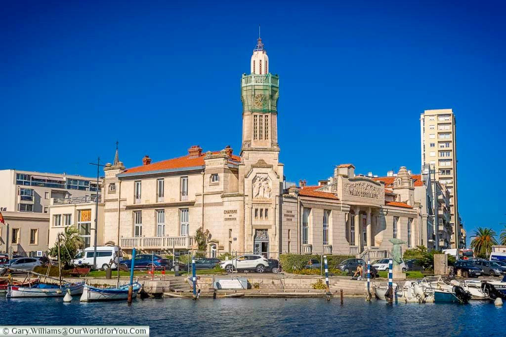 The striking Palais Consulaire in Sète, France, stands proudly along the waterfront with its ornate façade and red-tiled roof beneath a clear blue sky. This historic chamber of commerce building adds a touch of grandeur to the maritime charm of Sète’s bustling harbour.