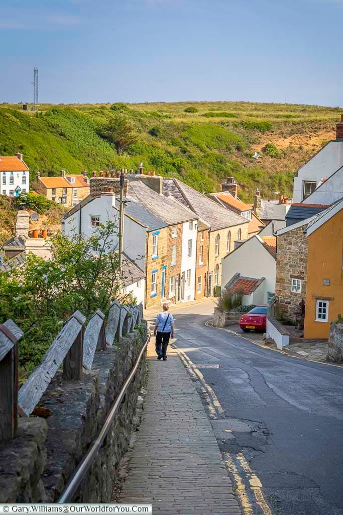 A scenic view down Staithes Lane reveals a collection of stone-built cottages nestled in a green hillside. This winding pathway is one of the village’s key routes down to the harbour.