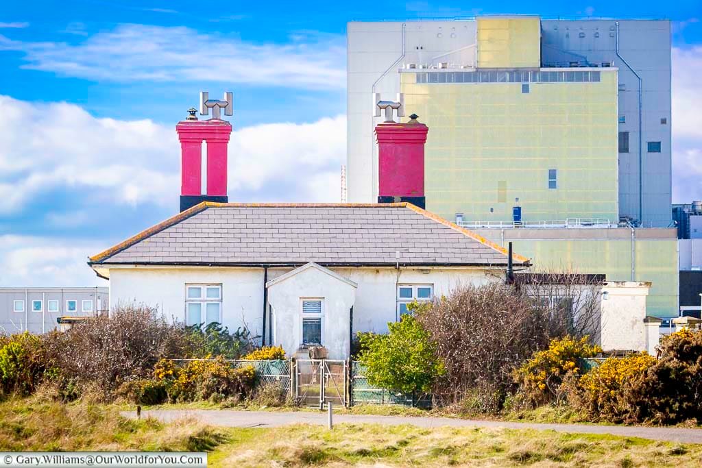 The Dungeness Nuclear Power Station rises behind a cottage with striking red chimneys on the Kent coast. This image captures the dramatic contrast between industrial architecture and the rugged natural landscape that defines Dungeness, one of England’s most distinctive coastal locations.