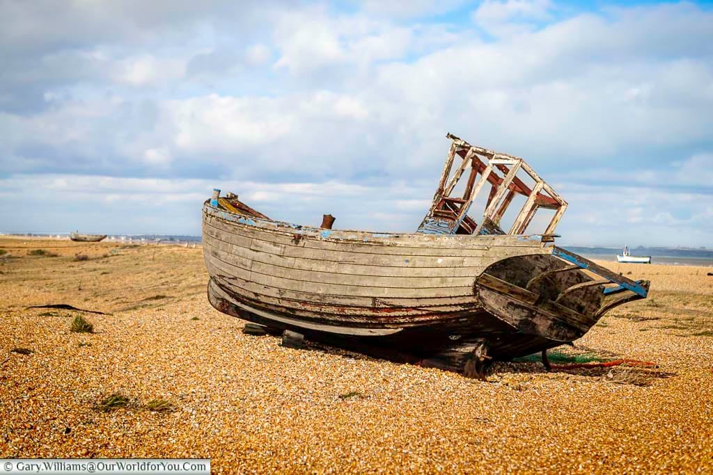 The same abandoned fishing boat at Dungeness, Kent, now faded and collapsing, lies quietly on the pebbled shore under a soft, overcast sky. This later photograph shows how the once vibrant vessel has deteriorated over time, reflecting the ever-changing coastal landscape of Kent.