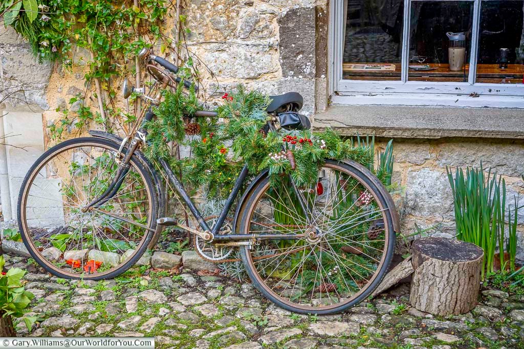A vintage bicycle decorated with Christmas greenery rests against a stone wall in the grounds of Ightham Mote. This charming festive display adds character to the historic Kent manor during the winter season.