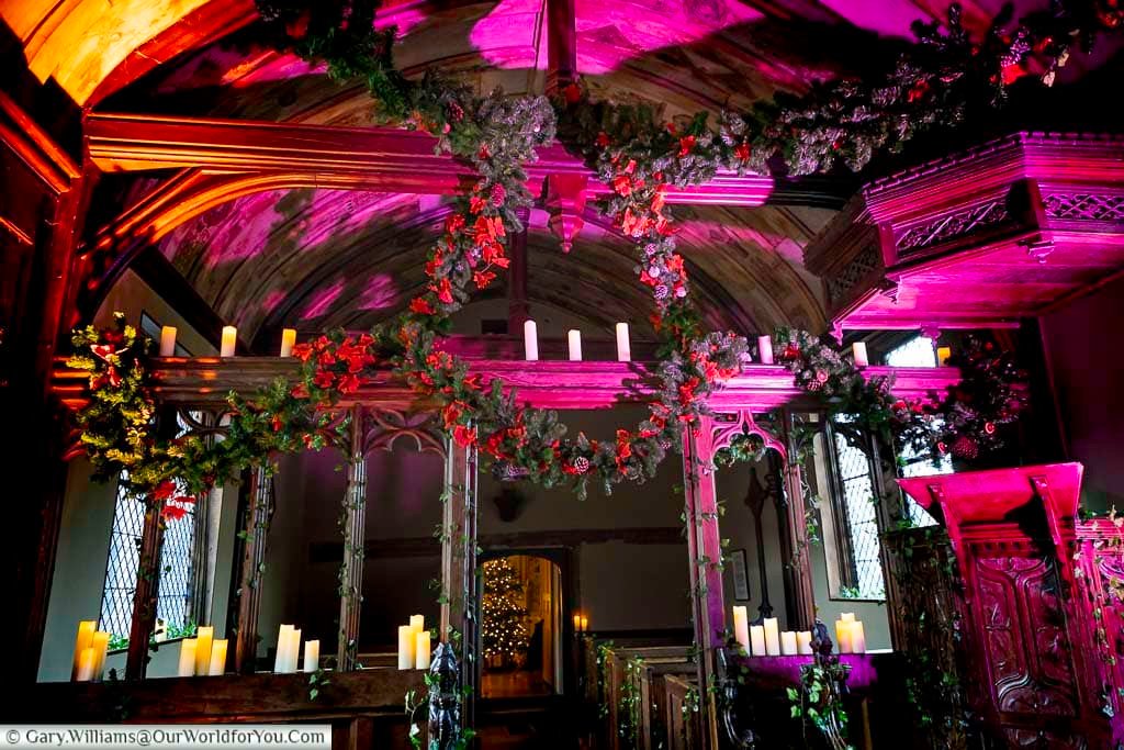 The New Chapel at Ightham Mote is adorned with festive garlands, candles, and dramatic coloured lighting. This atmospheric space highlights Christmas celebrations within the medieval National Trust property.