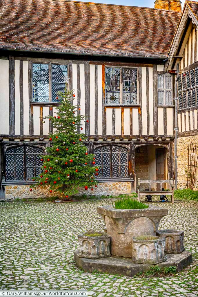 A decorated Christmas tree stands in the cobbled courtyard of Ightham Mote, framed by timber-framed walls and leaded windows. The festive scene adds seasonal charm to this historic Kent landmark.