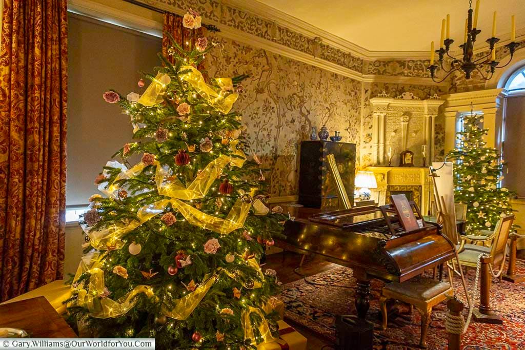 The Drawing Room at Ightham Mote is warmly decorated with a Christmas tree, antique piano, and period furnishings. Soft lighting and festive décor showcase the house’s historic elegance during the Christmas season.