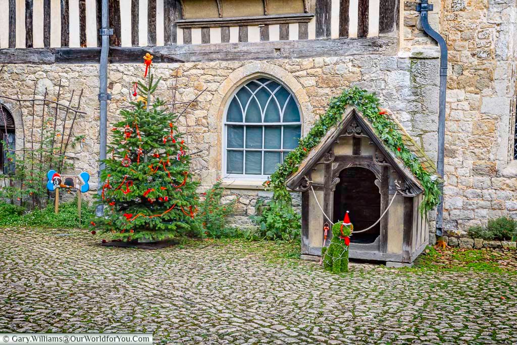 A festive Christmas tree and decorated dog kennel sit in the cobbled courtyard of Ightham Mote, adding a playful seasonal touch to the historic setting. This charming outdoor display highlights the estate’s attention to detail during the Christmas period.
