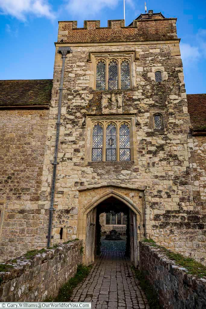 The medieval gatehouse entrance at Ightham Mote in Kent, featuring stone walls, leaded windows, and a cobbled walkway leading into the historic courtyard. This striking National Trust property showcases classic Tudor architecture and is one of the most atmospheric historic places to visit in Kent.
