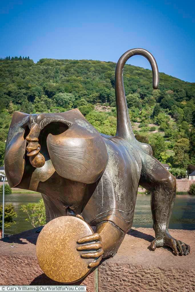 Bronze Heidelberg Bridge Monkey statue on the Old Bridge overlooking the River Neckar with wooded hills rising behind the historic old town. Quirky landmark sculpture in Heidelberg, Germany, offering scenic views of the river and Neckar Valley.