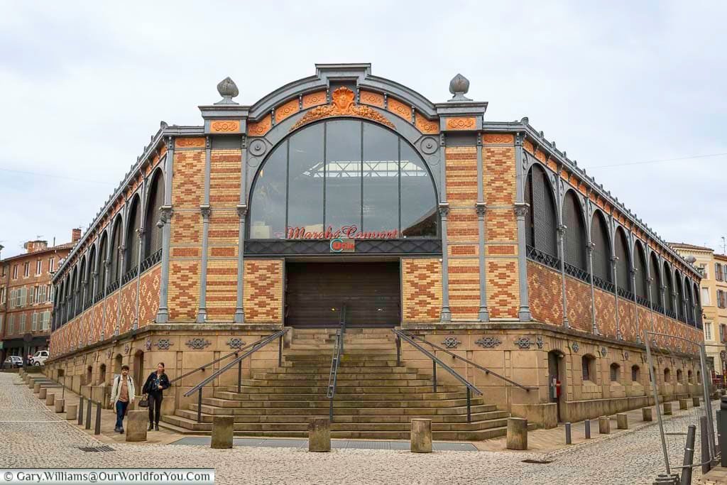 Exterior view of the Marché Couvert d’Albi, a striking 19th-century market hall built from red brick and iron with a grand central entrance. This historic market is a key landmark in Albi and a focal point of local daily life.