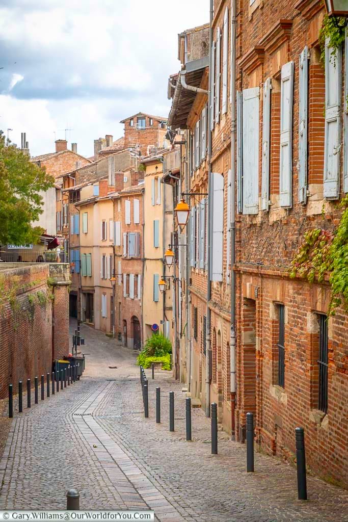 Quiet cobbled street in Albi lined with traditional brick townhouses and pastel shutters in the historic centre. This atmospheric lane captures the charm of Albi’s medieval streets and hidden corners in southern France.
