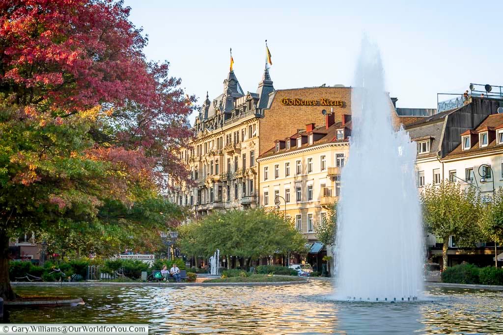 Fountain at Augustaplatz in Baden-Baden, surrounded by autumn trees and grand historic buildings in the town centre. This leafy square is a popular stop on a walking tour of Baden-Baden, blending nature with elegant urban design.