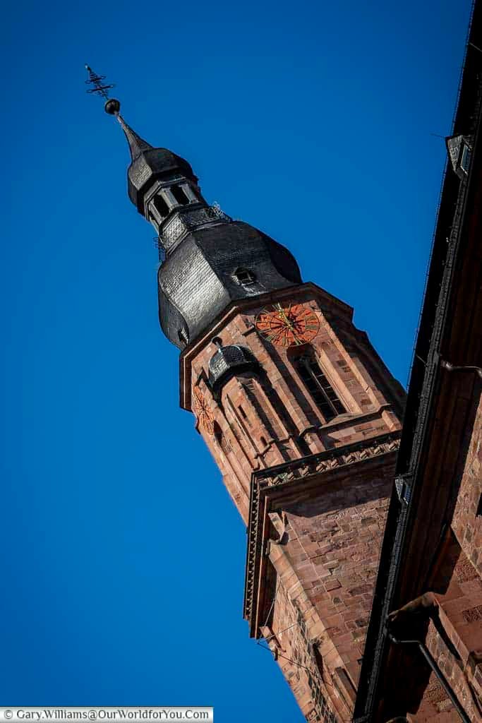 Close-up view of the baroque tower of the Church of the Holy Spirit set against a clear blue sky in Heidelberg’s old town. The red sandstone architecture and striking clock face make this landmark church a focal point of the historic centre.