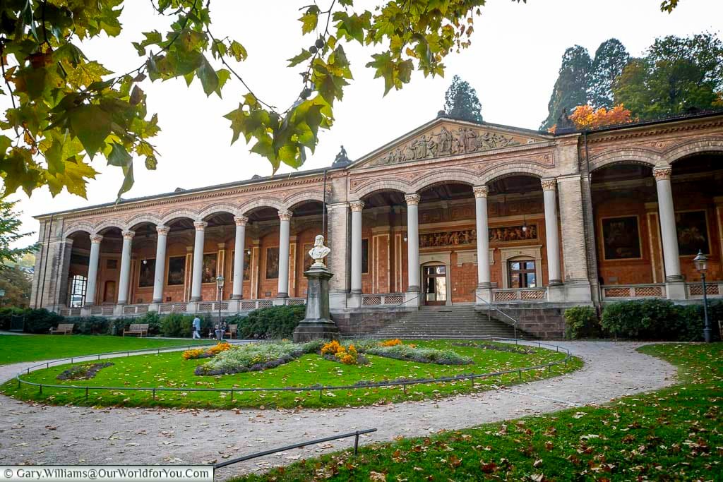 Exterior view of the Trinkhalle in Baden-Baden, set within manicured gardens and tree-lined paths. The elegant arcade reflects the town’s spa heritage and its reputation for refined leisure.