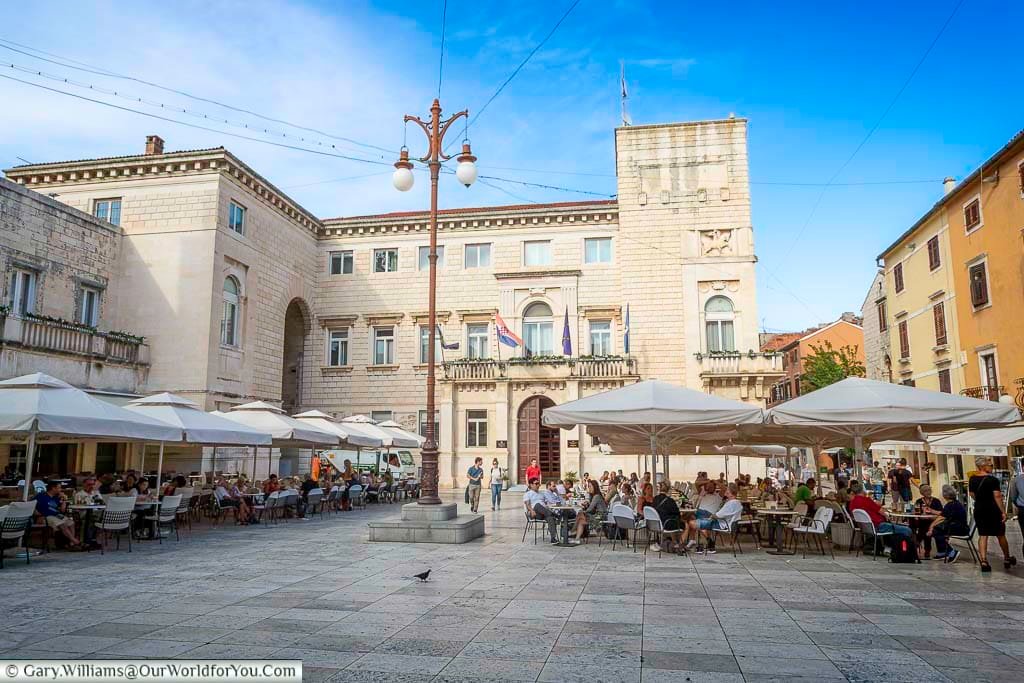 Families sitting at tables under parasols in People’s Square in the old town of Zadar