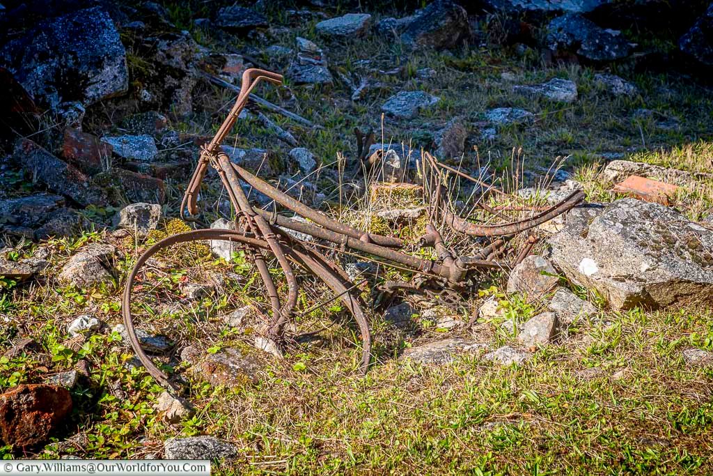 A rusted bicycle lies discarded in the grass among the ruins of Oradour-sur-Glane, France. Left behind after the 1944 massacre, it symbolises the sudden loss of everyday life in this preserved memorial village.