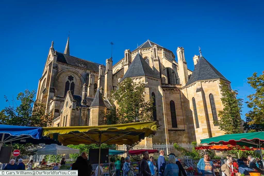 Shoppers browse the lively Saturday market in Bergerac, Dordogne, with colourful stalls set beneath the impressive stone church. This bustling market scene captures the authentic atmosphere of a traditional French town in southwest France.